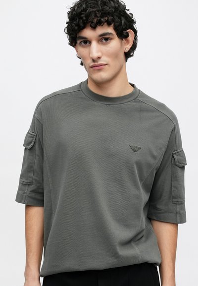 Šedé bavlněné tričko s krátkými rukávy, kulatým výstřihem, nenápadným logem na hrudi a kapsami ve stylu cargo na rukávech.