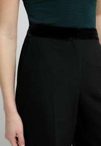 Zwarte, op maat gemaakte broek met een fluwelen tailleband, met een gladde textuur en zijzakken, gecombineerd met een donker groen, sprankelend topje.