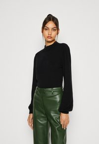 Black knit sweater with a high neckline and puffed long sleeves, paired with high-waisted green faux leather trousers.