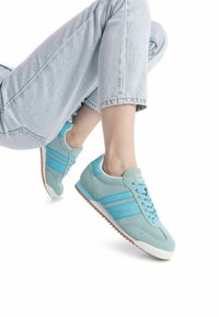 Zapatillas de ante azul claro con rayas azul oscuro, suela de goma blanca y suela exterior texturizada marrón. Cordones en un tono azul a juego.