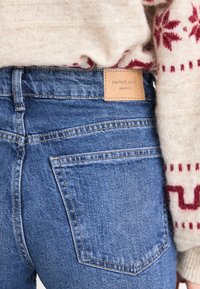 Τζιν με μπλε πλύσιμο, με απλό σχέδιο, ραμμένες τσέπες και καφέ ετικέτα που γράφει "τέλεια τζιν".