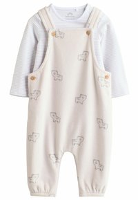 Fleece haalaree karhun kuviolla vaalean beige värissä, jossa on olkaimet ja puunappeja yksityiskohtana. Pitkät hihat valkoisessa ja harmaassa raidallisessa paidassa alla.