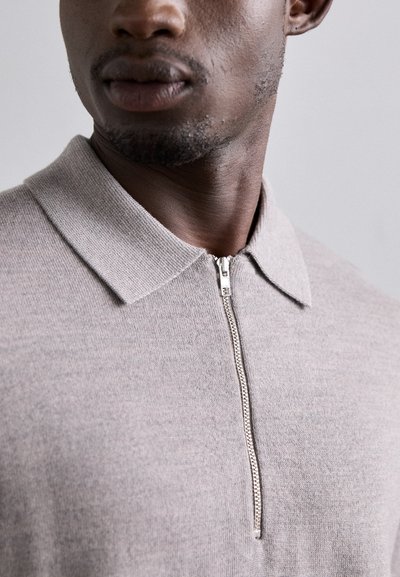 Hellgraues, reißverschlussfreies Polo-Shirt mit Kragen und feiner Strickstruktur. Der Reißverschluss an der Vorderseite sorgt für Funktionalität und einen modernen Akzent.