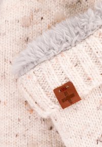 Knitted sweater in off-white with flecks of orange, featuring a light gray fur collar and a brown leather tag with a logo. Textured fabric.