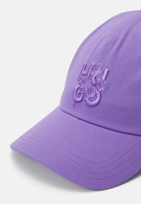 Fialová baseballová kšiltovka vyrobená z texturované látky, s vyšitým květinovým logem na levé přední straně. Design s ohnutým kšiltem.