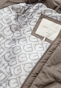 Bruine gewatteerde jas met een rits, met een witte voering bedrukt met grote letters en een genaaid label met de tekst "FREE/QUENT SMALL."