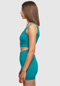 Tyrkysový športový outfit obsahujúci priliehavý crop top so širokými ramienkami a zodpovedajúce vysoké šortky, vyrobené z hladkého, elastického materiálu.