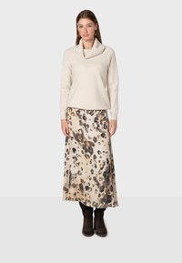 Pull créme à col drapé associé à une jupe beige avec un imprimé animal noir et marron. Le mannequin porte des bottes noires jusqu'aux genoux.