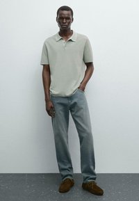 Lys grå kortærmet polo skjorte med tre knapper, parret med falmede blå jeans og brune sko med snørebånd. Enkel, afslappet design.