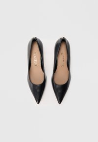 Escarpins en cuir noir à bout pointu, avec une texture lisse et un logo "GUESS" doré sur une semelle intérieure beige.