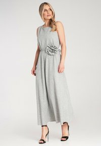 Szara, bezrękawnikowa sukienka maxi z miękkiego materiału, z kwiecistym akcentem w talii i zwiewnymi, szerokimi nogawkami. Całość uzupełniają sandały na obcasie.
