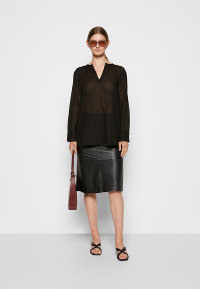 Blusa preta transparente de mangas longas com decote em V, combinada com uma saia justa de couro preto. Os acessórios incluem óculos de sol redondos e com cor e uma bolsa bordô.