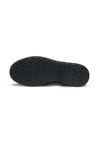 Semelle en caoutchouc noir d'une chaussure avec un motif de bande de roulement en zigzag, vue du dessous sur fond blanc.