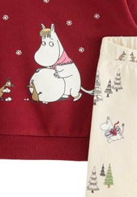 Červená mikina s ilustracemi Moominů, žebrovaný lem; krémové kalhoty s hravými scénami Moominů a stromy. Bavlněný materiál.