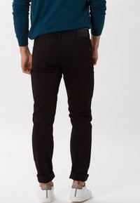 Jeans neri slim-fit con una texture liscia e tasche posteriori, indossati con i risvolti e sneakers bianche.