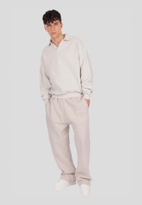 Világos bézs garbónyakú hosszú ujjú pulóver, amelyhez passzoló bézs melegítőnadrág van párosítva. A sportcipők fehérek. Egyszerű kialakítás, minimális díszítéssel.