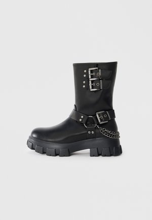 Czarna gumowa boots z srebrnymi klamrami i ćwiekami, teksturowana skórzana wykończenie, masywna platforma oraz detal w postaci łańcucha po boku.