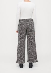 Personne portant un pantalon large imprimé zèbre, un haut blanc à manches longues et des bottines noires à talons, vue de dos.