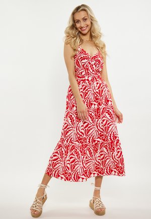 Maxikleid mit rotem Blumenmuster, Spaghetti-Trägern, weit ausgestelltem Saum und Rüschensaum. Kombiniert mit braunen, geschnürten Keilsandalen.