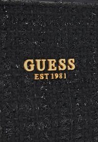 Czarna tkana tekstylia z błyszczącymi nićmi, z logo "GUESS" w kolorze złotym oraz "EST 1981" w wyraźnej czcionce. Teksturowana powierzchnia z wyraźnymi wzorami.