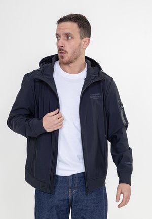 Marineblauwe hooded jack met een ritssluitingszak op de linkermouw en een logo op de borst. Gemaakt van glad, lichtgewicht materiaal; ontspannen pasvorm.