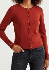 Röd knäpp cardigan i mjukt stickat tyg. Har rund hals, långa ärmar och knappar i guldton framtill och på manschetterna.