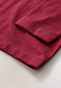 Burgundi színű pamut ing anyag összehajtva, sima textúrával és tiszta szegéllyel. Rövid ujjakkal és minimális varrási részletekkel rendelkezik.
