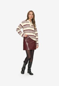 Camicia a maniche lunghe color crema con strisce bordeaux, abbinata a una mini gonna in pelle bordeaux lucida e stivali neri al ginocchio.