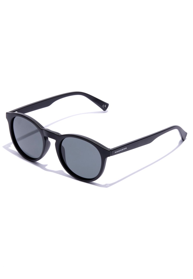 Round-frame sunglasses with a matte black plastic frame and grey lenses. Features subtle branding on the side of the arm.