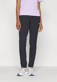 Černé sportovní kalhoty s keprovým střihem, vyrobené z lehkého materiálu. Na stehně je malá značka. Doplněny o šedé a modré sportovní boty.