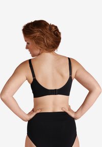 Svart trådlös bh med justerbara remmar, slät tyg och en krokförslutning på baksidan. Åtföljd av svarta höga trosor.