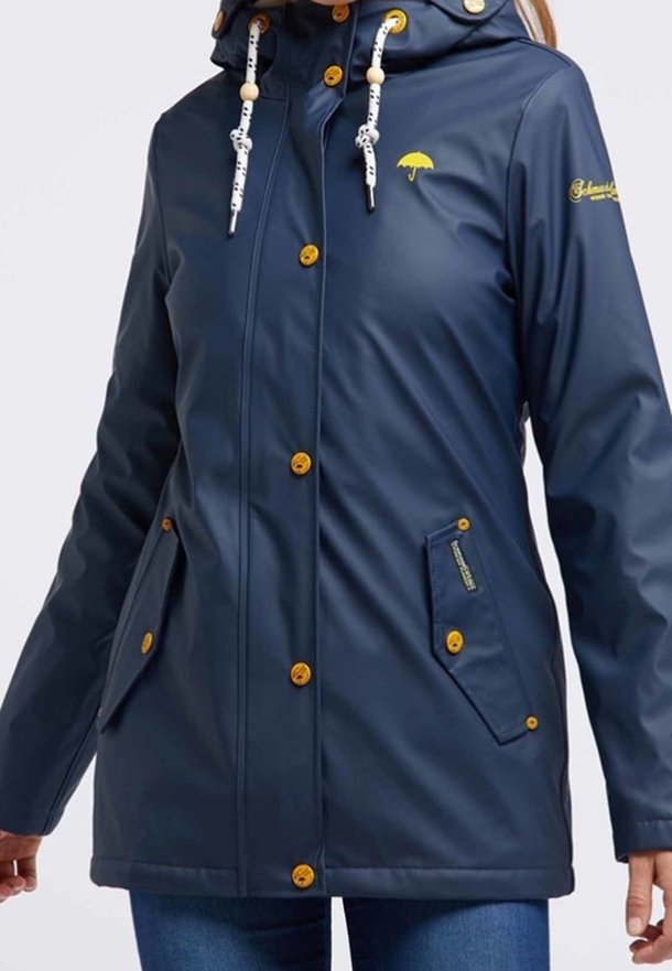 Tmavě modrá voděodolná bunda s kapucí, se žlutými knoflíky a doplňky. Obsahuje dvě boční kapsy a malou logu deštníku.