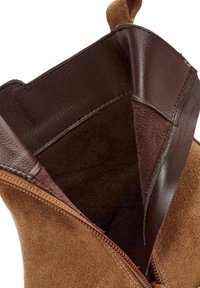 Stivaletto in suede marrone con interno in pelle marrone, dotato di zip e una linguetta sul retro. Texture morbida, vestibilità aderente.