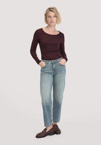 Bourgondische lange mouwen top gecombineerd met lichtgewaste, losse jeans en bruine instap schoenen met een textuurpatroon.