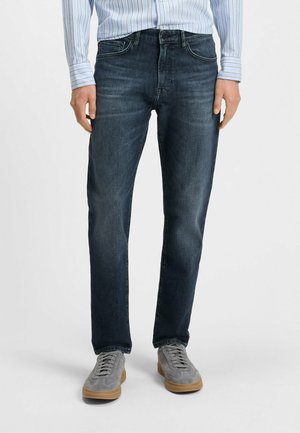 Dark blue denim jeans with a straight fit, featuring a classic five-pocket design and subtle fading. Worn with a striped long-sleeve shirt.