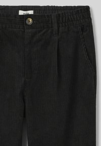 Pantalon en velours côtelé noir présentant une texture côtelée verticale, une taille élastique, des poches frontales et une fermeture à bouton.