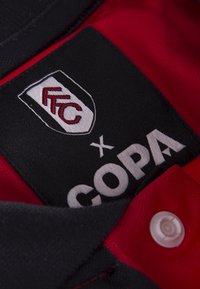 Rood en zwart jersey met een kraag, voorzien van een geborduurd logo patch met de branding "FFC" en "COPA". Plastic knoop bij de opening van de kraag voor sluiting.