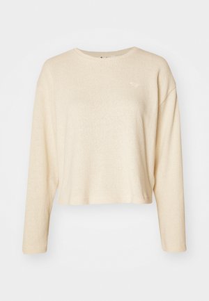 Krämfärgad korttröja med långa ärmar, gjord av strukturerat tyg. Har en liten, diskret logotyp på bröstet och en rundad halsringning.