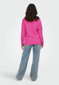 Rosa Strickpullover mit geripptem Muster, Rundhalsausschnitt und lässigem Schnitt, kombiniert mit hellblauen Jeans mit weitem Bein und weißen Sneakers.