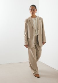 Μπέζ ταγέρ σακάκι και ταιριαστές φαρδιές παντελόνες, με μια υφασμάτινη ελαφριά μπλούζα από κάτω. Οι μυτερές μπέζ γόβες ολοκληρώνουν το σύνολο.