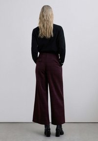 Pantalones de cuadros burdeos de pierna ancha con una cintura alta, que cuentan con bolsillos laterales y un bolsillo trasero, hechos de una tela suave.
