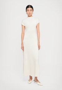 Witte, aansluitende maxi-jurk met korte mouwen, geribbeld patroon en een rechte silhouette. Gecombineerd met crèmekleurige, puntige schoenen.