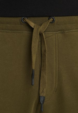 Pantalons de survêtement vert olive avec une taille côtelée noire, cordon de serrage réglable avec embouts noirs et poches latérales cousues.