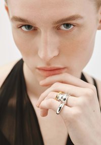 Anillos de metal plateado y dorado llevados en los dedos, con un diseño elegante y retorcido que presenta una textura suave y un acabado pulido.