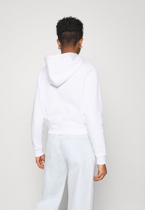 Vit kortärmad hoodie med dragsko i huvan, ribbade muddar och fåll, tillsammans med ljusblå hög midja jeans. Slät textur.