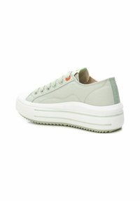 Zapatillas de lona verde claro con suela de goma blanca gruesa, con lados texturizados, cordones redondos y un pequeño acento naranja cerca de los ojales.