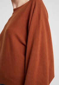 Pullover in Rostfarbe mit entspannter Passform aus strukturiertem Stoff; verfügt über einen abgerundeten Ausschnitt und überschnittene Schultern für einen modernen Look.