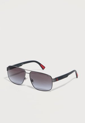 Sonnenbrille im Aviator-Stil mit schwarzem Metallrahmen, grauen Verlaufsgläsern, schwarzen Bügeln mit roten Akzenten und der "Polo"-Markierung an den Bügelenden.