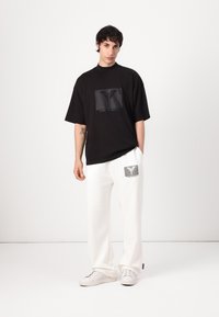 Zwart oversized t-shirt met een vierkant grafisch logo, gecombineerd met witte sweatpants met een bijpassende logopatch en witte sneakers.