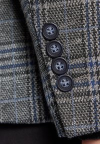 Szaro-niebieska tkanina w kratę o teksturowanym wykończeniu; posiada pięć ciemnoniebieskich guzików na mankietach, prezentujących szczegółowe przeszycia.